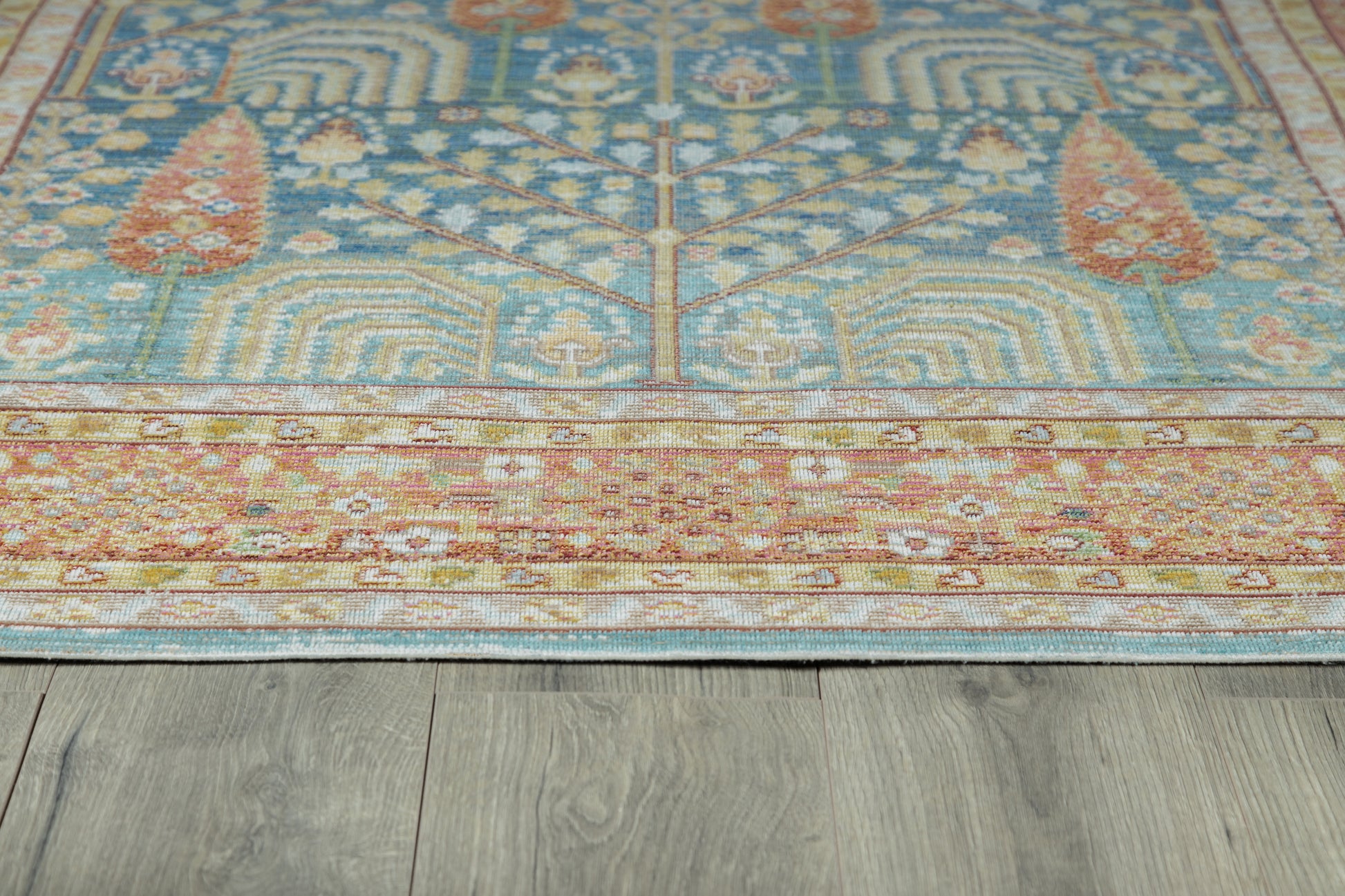 Blue oriental rug with cream floral motifs and a rust-red border on gray wood floor.