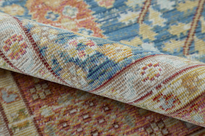 Close-up of a rolled, multicolor woven rug with blue, cream and pink-yellow floral motifs.
