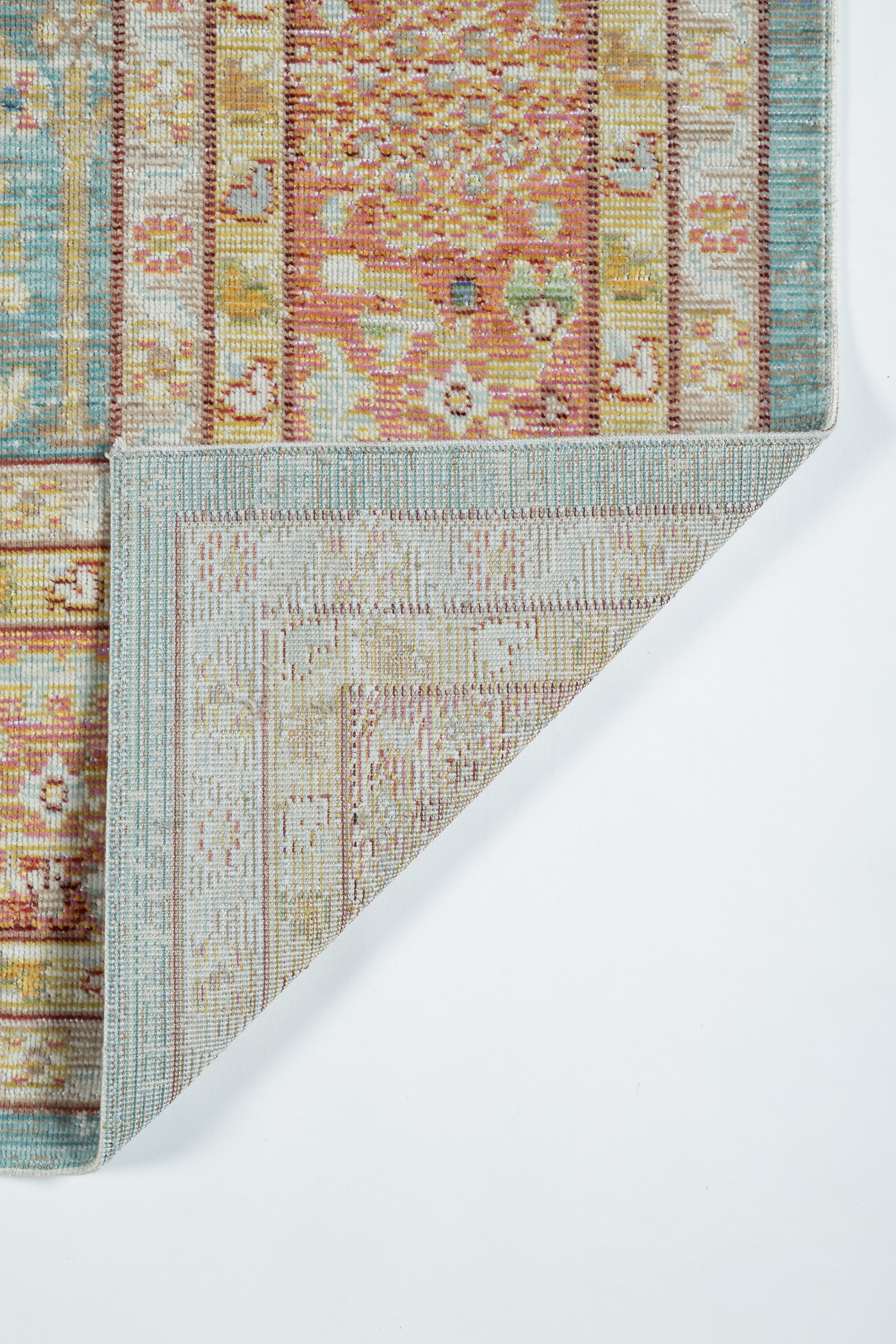 Colorful patterned rug with coral, pink, teal and beige tones; folded corner reveals pale blue border on reverse.
