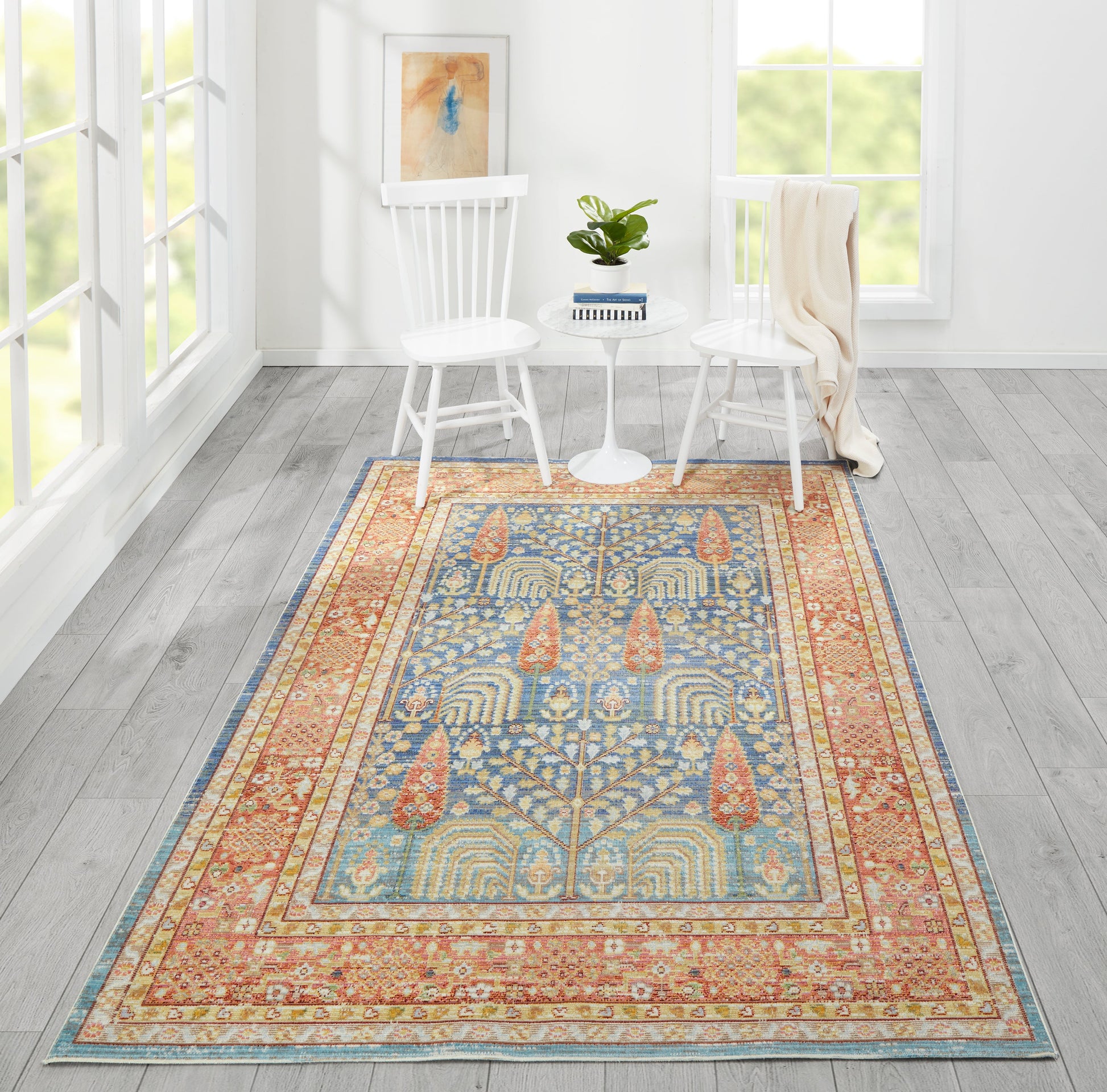 Rectangular oriental-style rug in blue, gold and coral with intricate border, in a white living room with two white chairs.