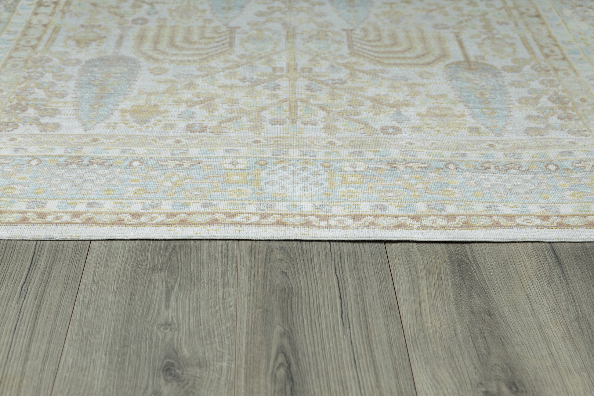 Rectangular area rug in cream and pale blue with ornate floral border, laid over gray wooden floor.