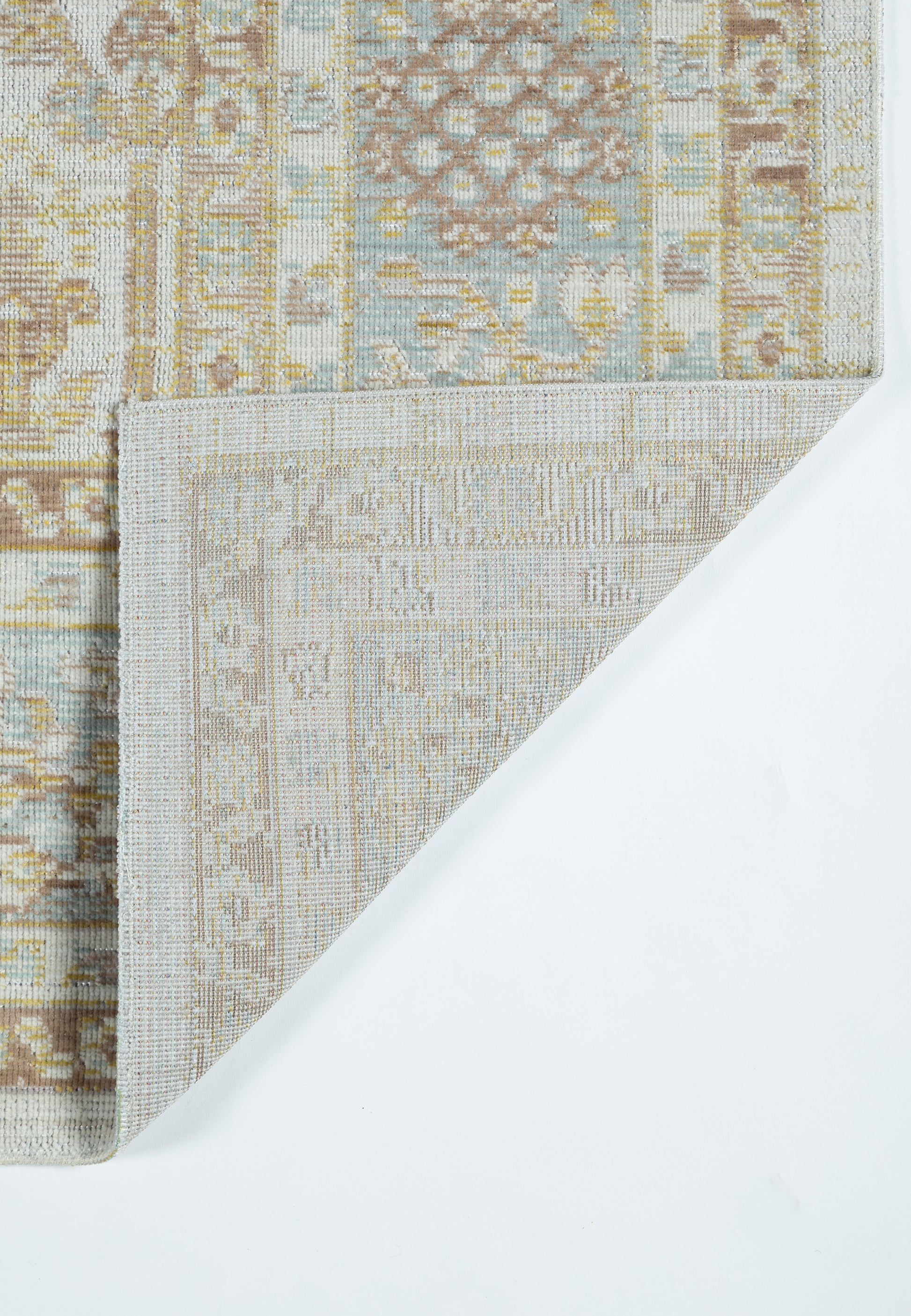Pastel beige and blue patterned rug with geometric motif, folded corner reveals lighter underside.