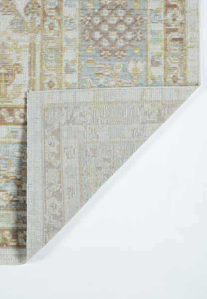 Pastel beige and blue patterned rug with geometric motif, folded corner reveals lighter underside.