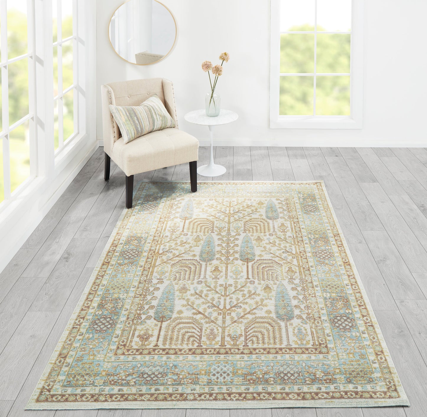 Beige oriental rug with blue accents in a sunlit living room beside a beige upholstered chair and round side table.