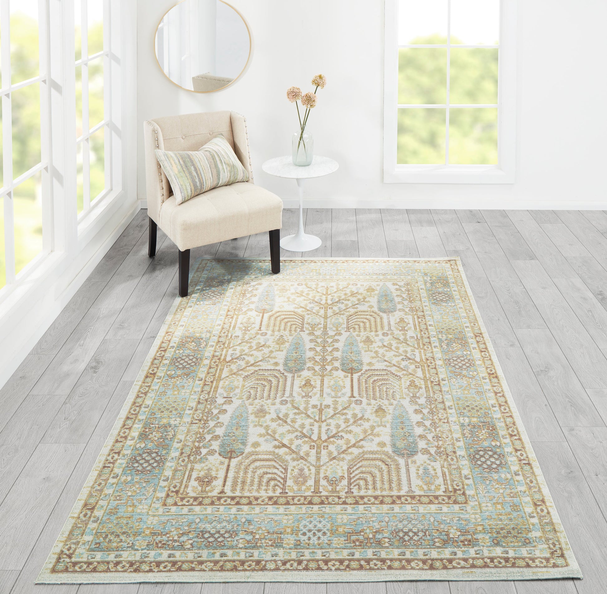 Beige oriental rug with blue accents in a sunlit living room beside a beige upholstered chair and round side table.