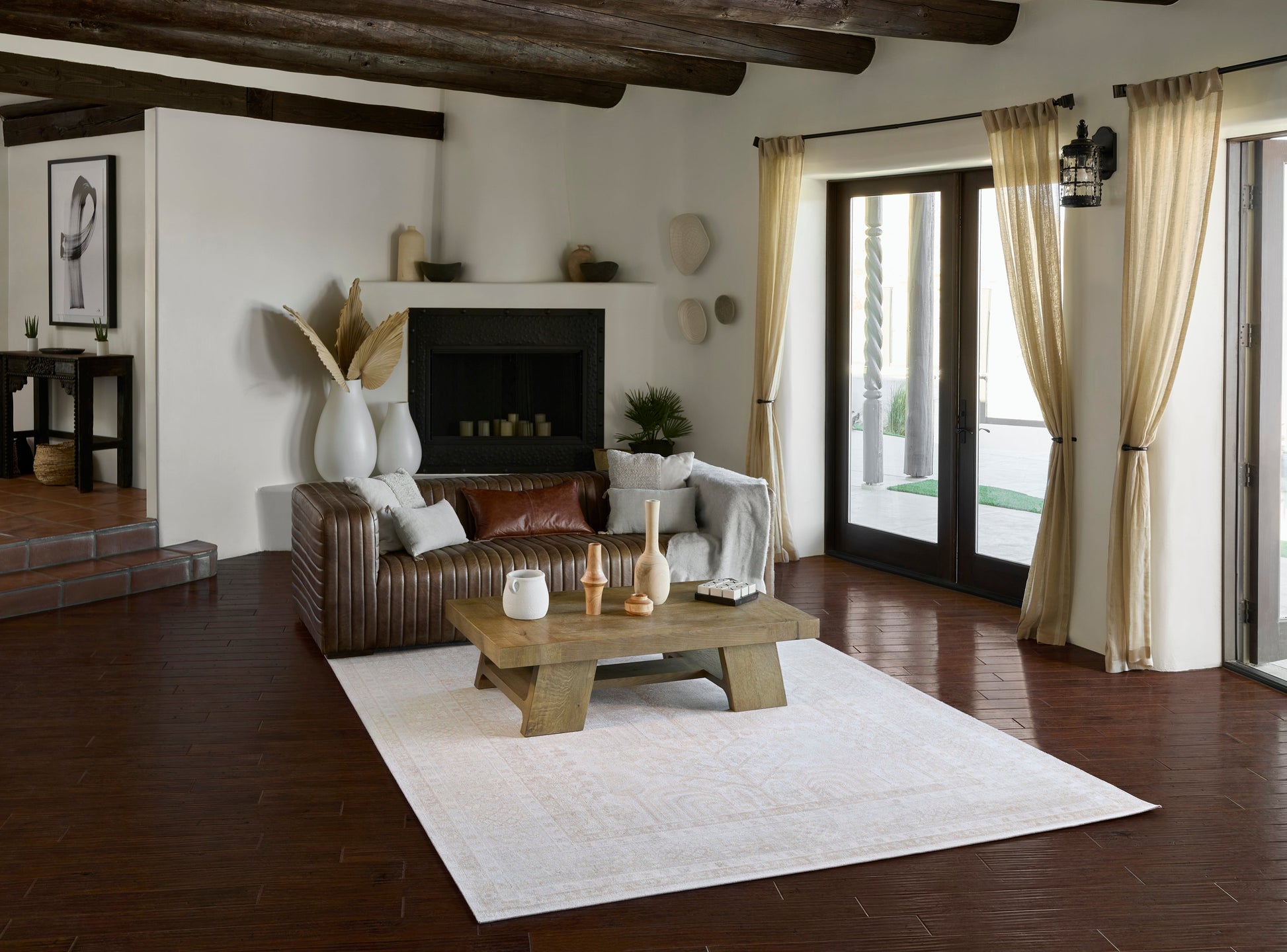Rustic-modern living room with dark wood beams, white walls, brown leather sofa, angular wood coffee table, fireplace.