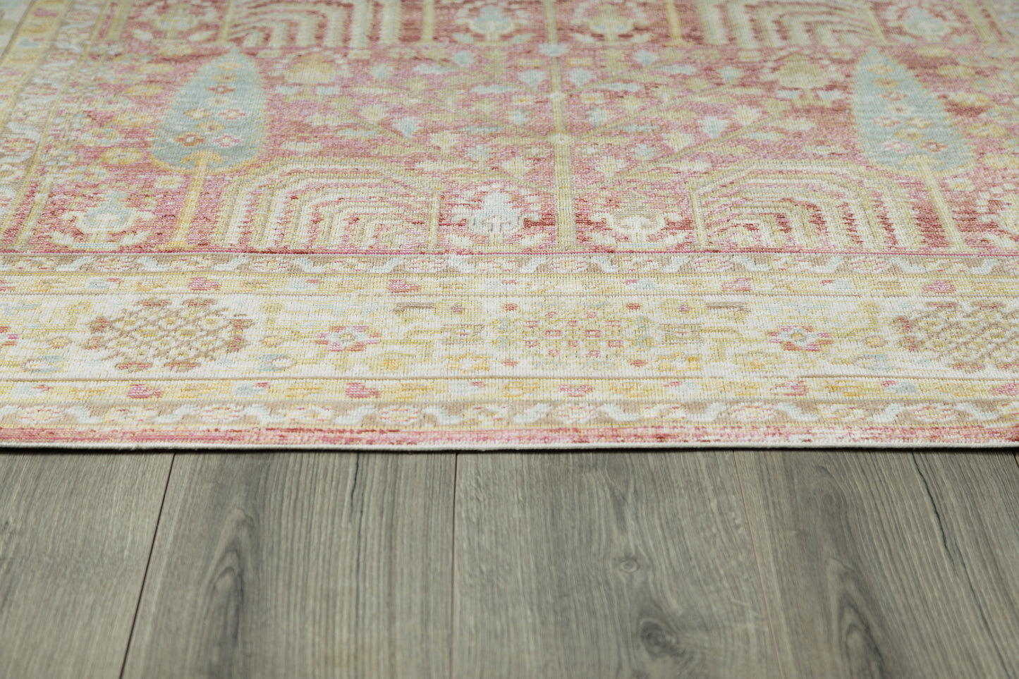 Pink and cream oriental-style area rug with geometric motifs and blush tones, laid on gray wood flooring.