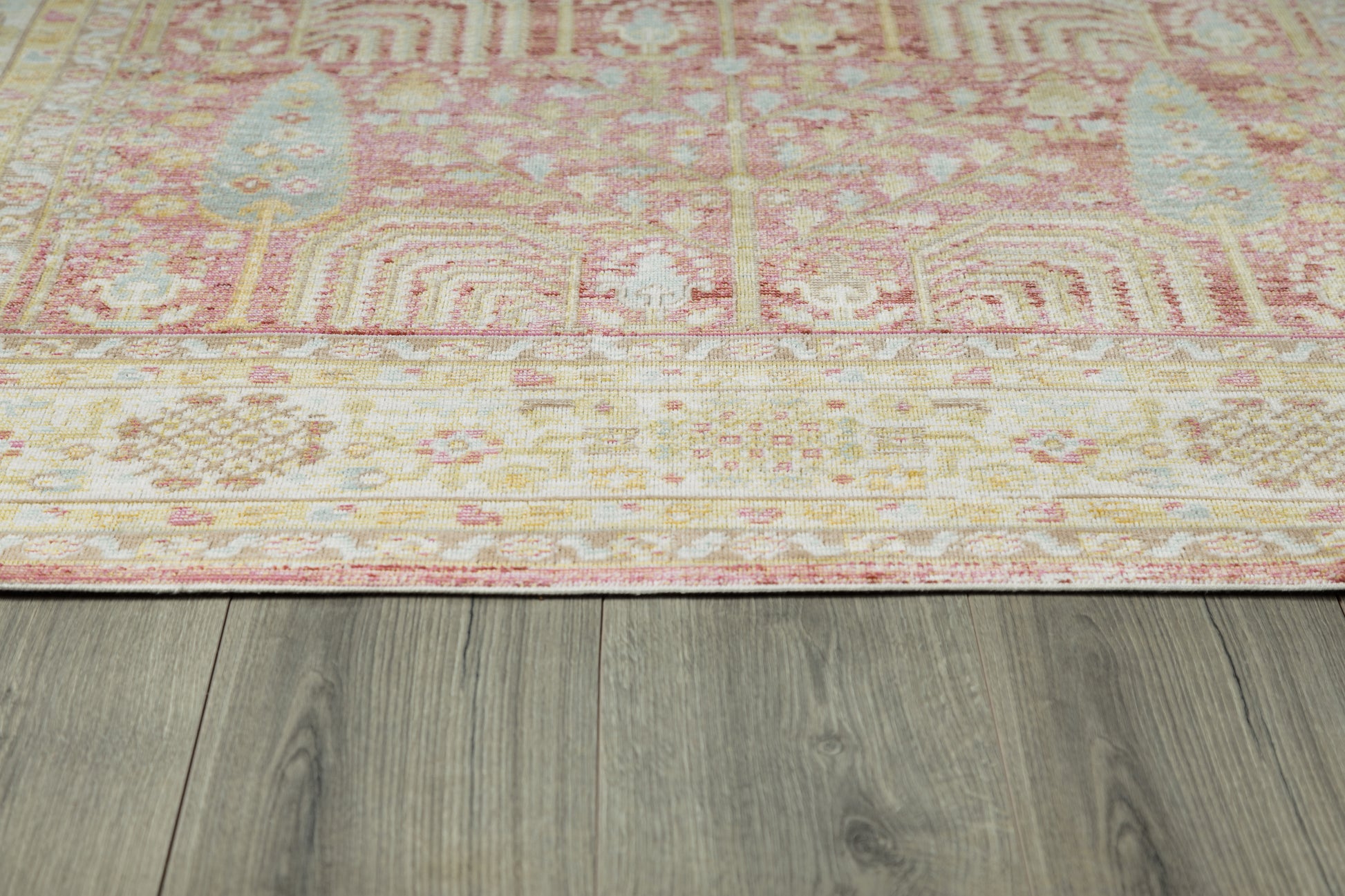 Pink and cream oriental-style area rug with geometric motifs and blush tones, laid on gray wood flooring.