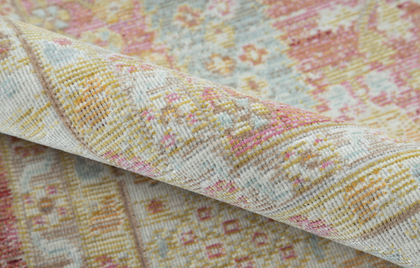 Pastel woven rug with pink, yellow, blue floral-geometric motif; folded edge on soft vintage textile.