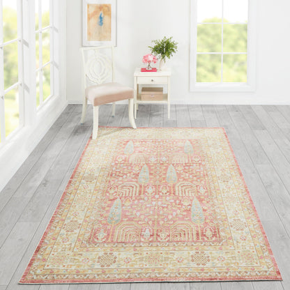 Soft peach-pink oriental rug with cream border on light gray wood floor, beside a white chair and table with pink flowers.