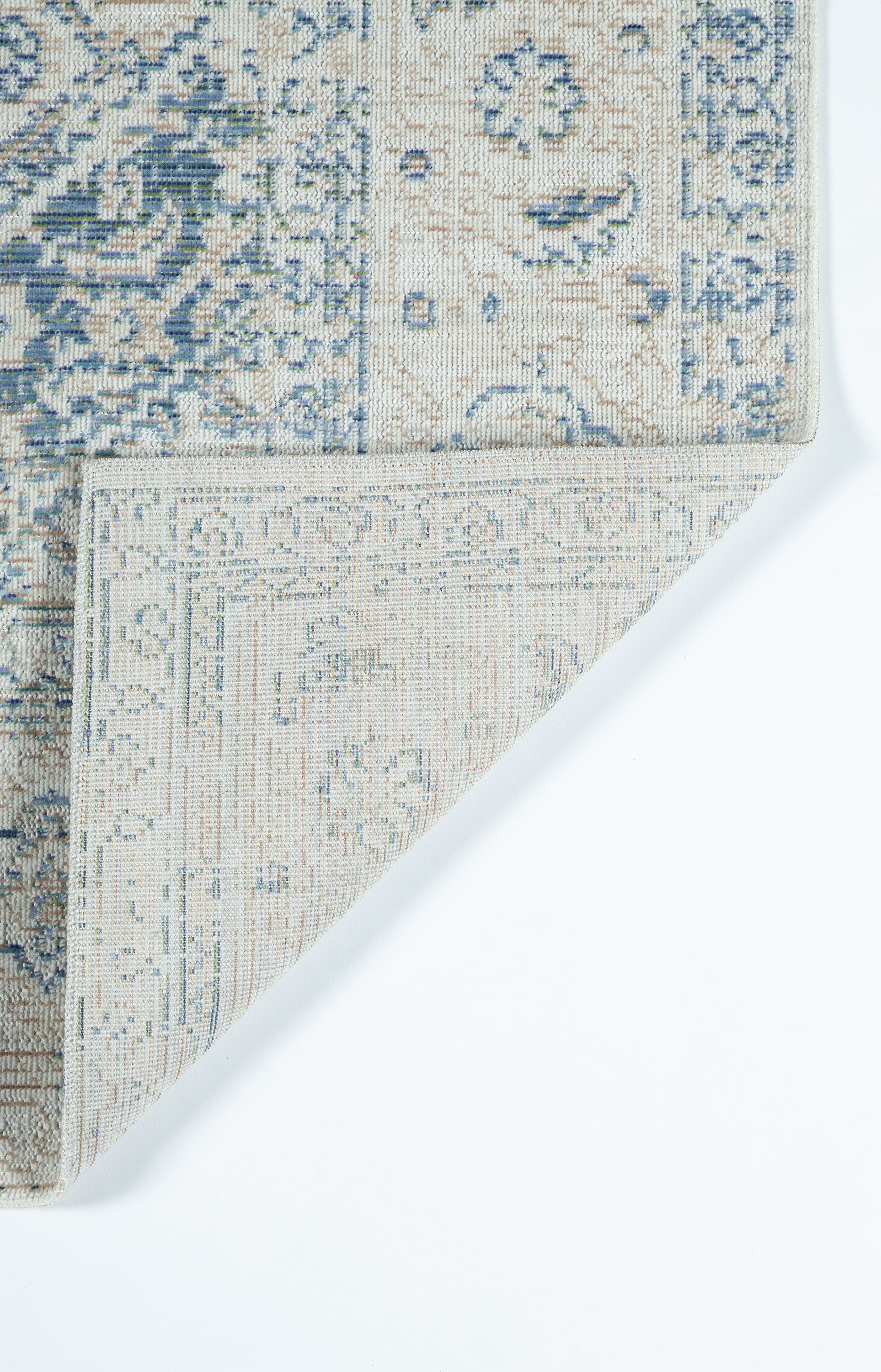 Blue and ivory patterned rug with ornate motif; corner folded to reveal beige underside.