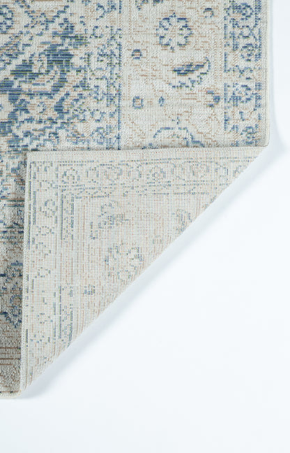 Blue and ivory patterned rug with ornate motif; corner folded to reveal beige underside.