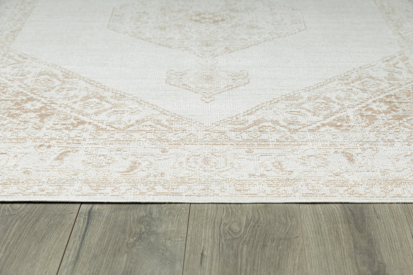 Cream beige area rug with a subtle faded medallion pattern and decorative border on gray wood floor