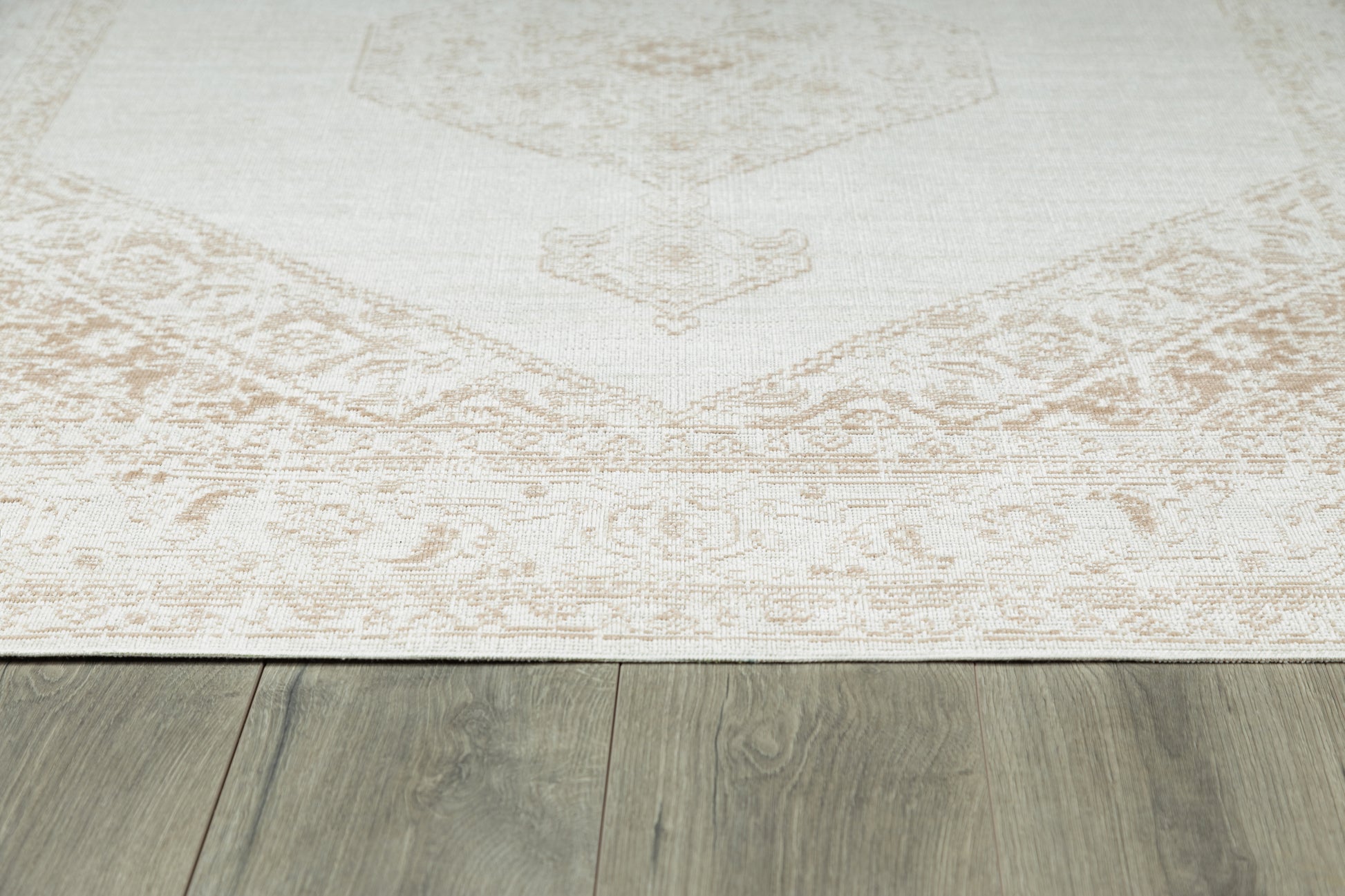 Cream beige area rug with a subtle faded medallion pattern and decorative border on gray wood floor