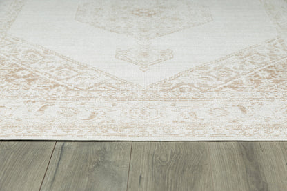 Cream beige area rug with a subtle faded medallion pattern and decorative border on gray wood floor