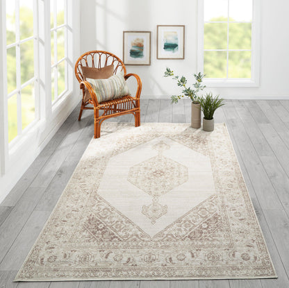 Bright living room with a beige medallion area rug, rattan chair, striped cushion, potted plants & framed wall art.
