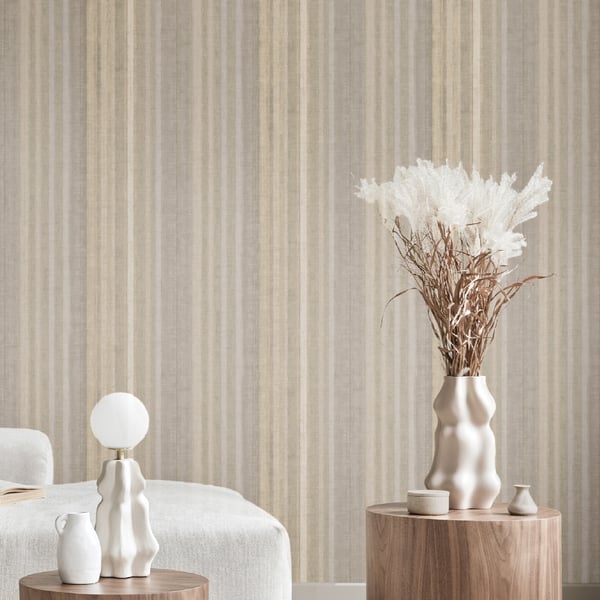 Beige striped wallpaper with white sculptural vases and pampas grass on round wooden stands, cozy bedroom decor