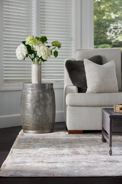 Industrial metal barrel side table with a tall metallic vase of white hydrangeas beside a light gray sofa.