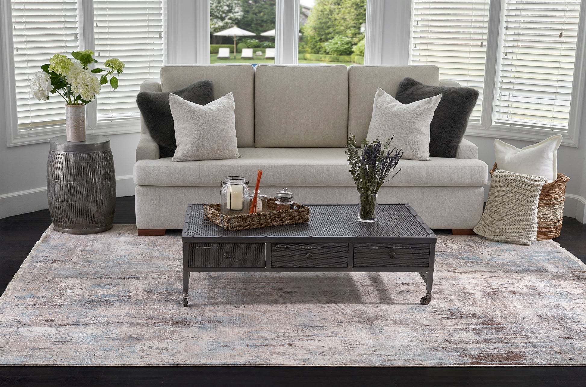 Neutral living room: beige sofa, rectangular dark wood coffee table with drawers, blue-gray area rug, and greenery.
