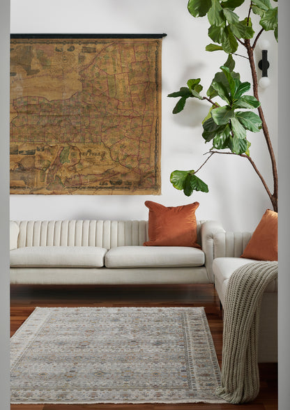 Cream sofa with orange cushions, knitted throw, vintage map wall art, tall fiddle-leaf fig, and a neutral patterned rug.