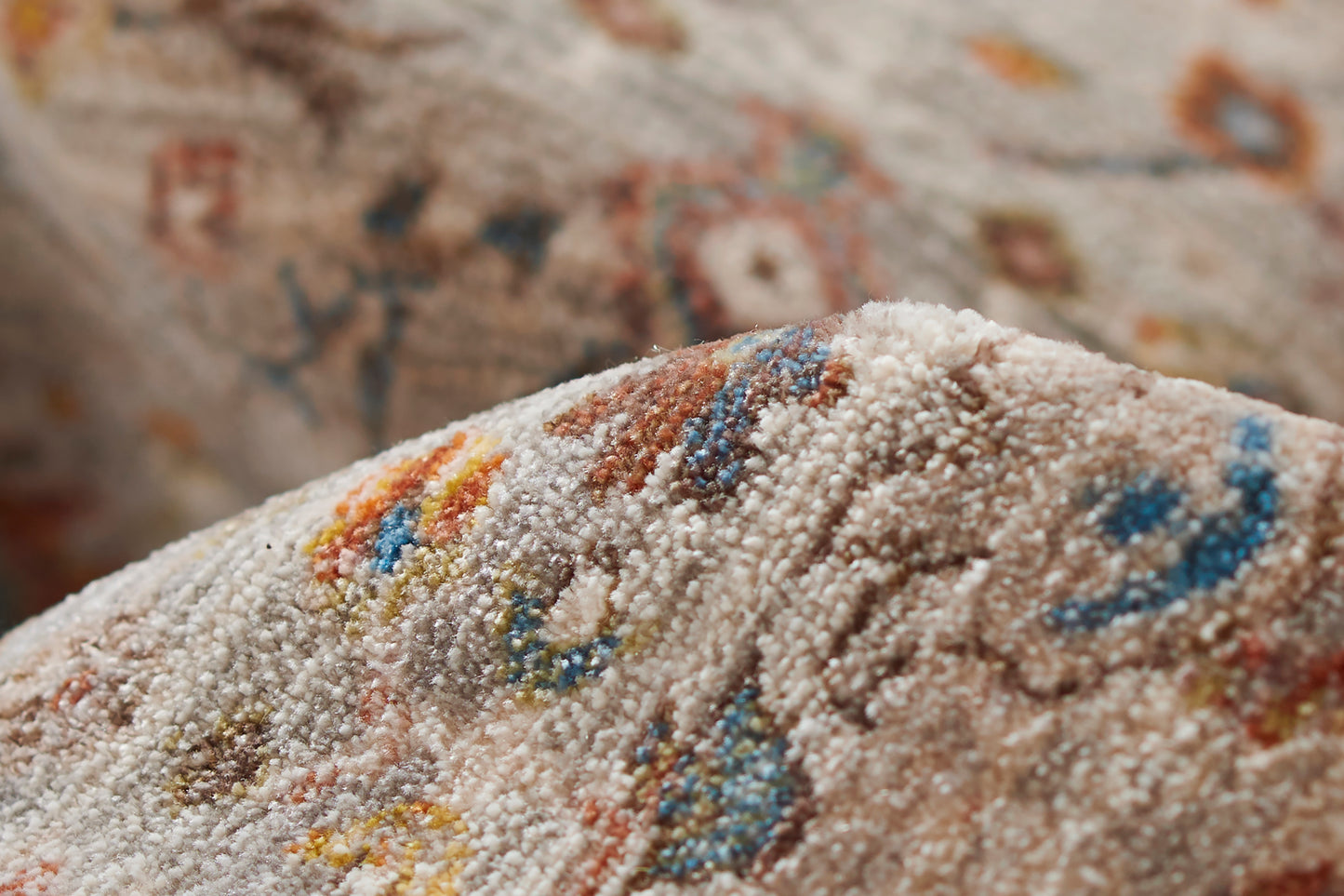 Beige tufted rug close-up with multicolor speckled pattern (blue, orange, red, yellow); soft cozy decor piece.
