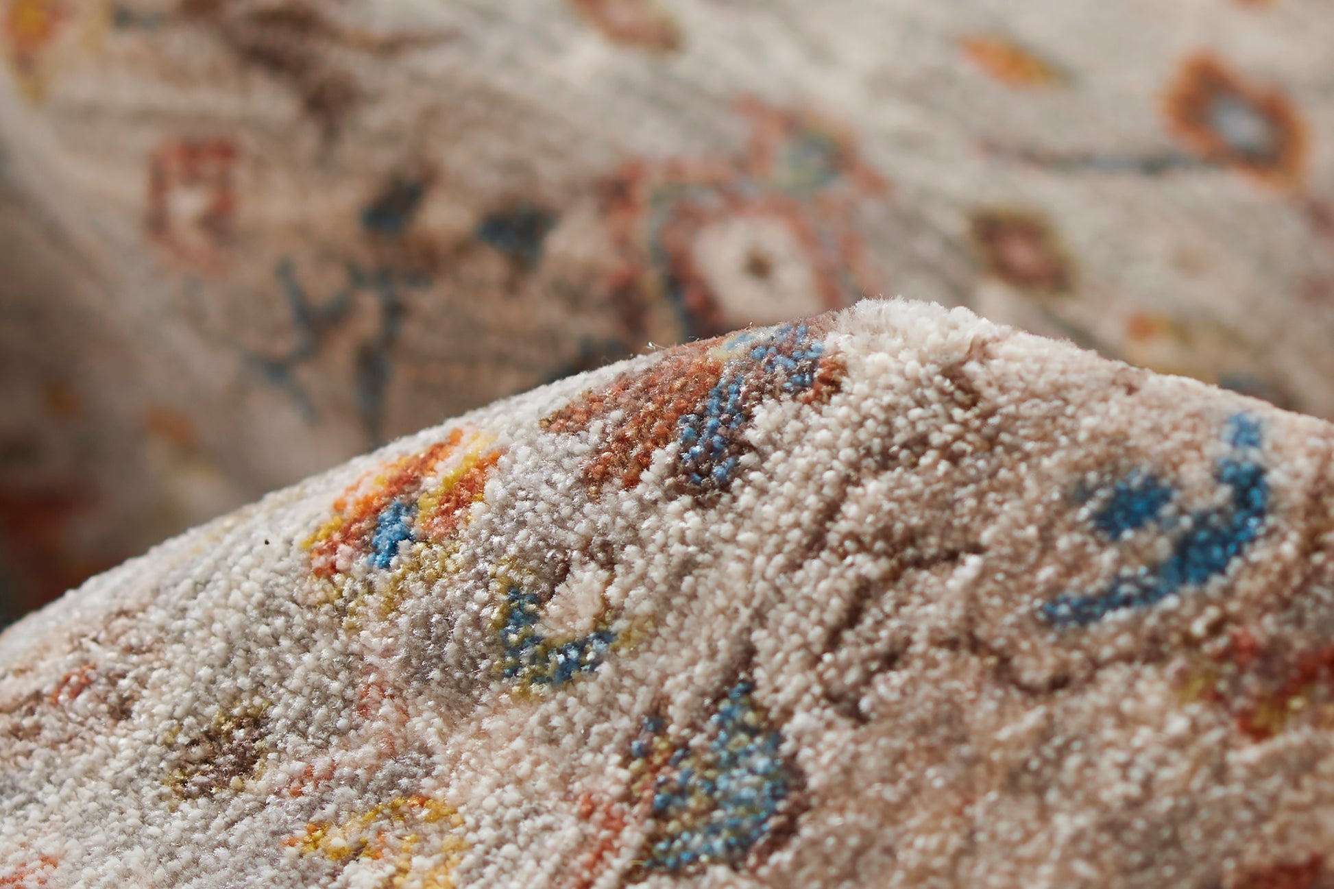 Beige tufted rug close-up with multicolor speckled pattern (blue, orange, red, yellow); soft cozy decor piece.
