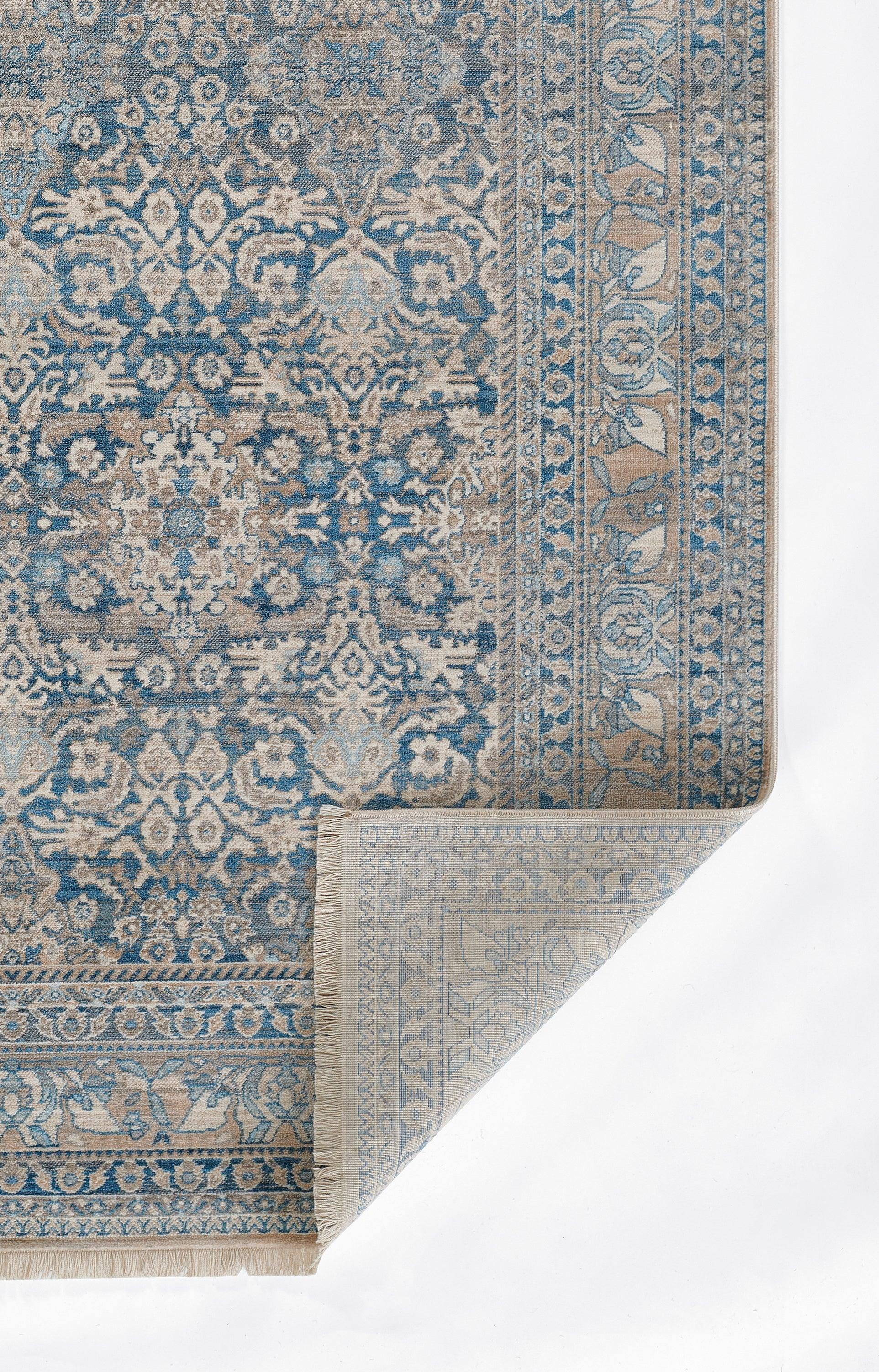 Blue ornate rug with floral medallions and beige border, folded corner showing lighter underside.