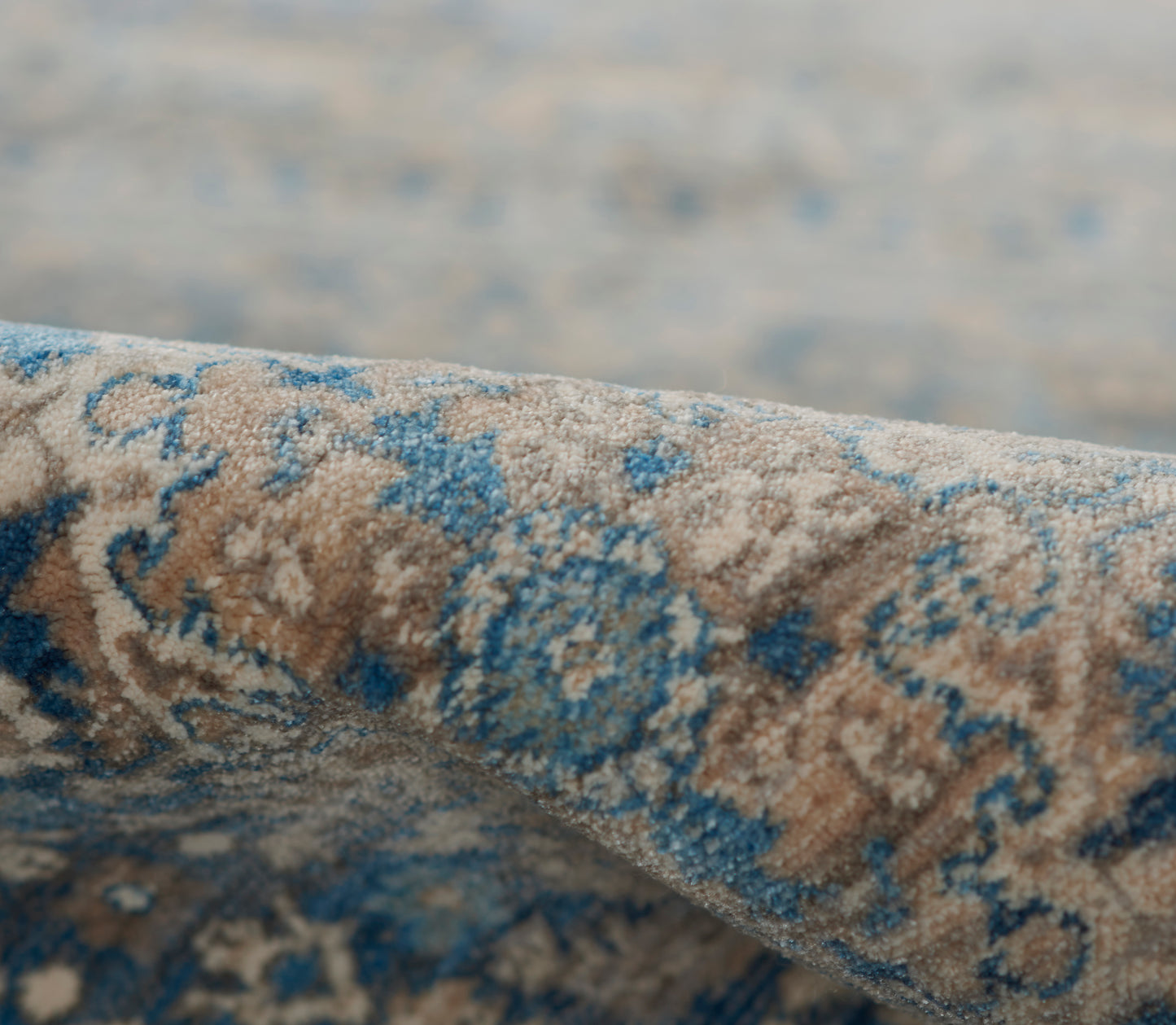 Close-up of blue & beige patterned rug with floral motif, slightly rolled edge.