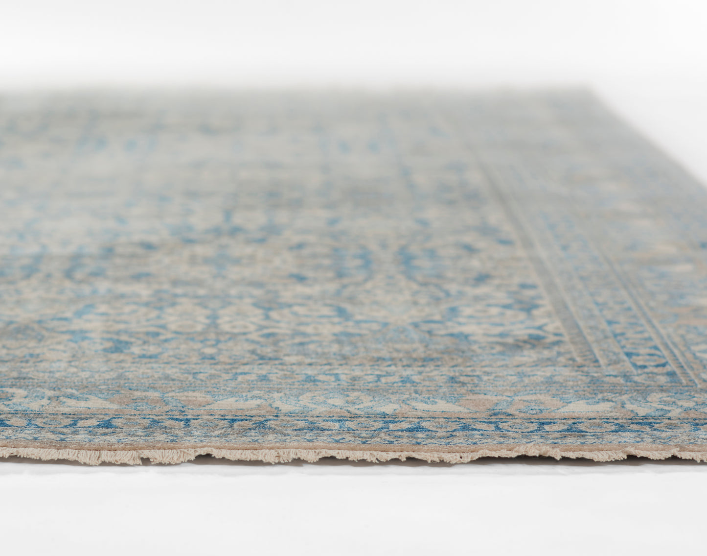Blue and beige oriental-style rug with a faded pattern and fringed edge.
