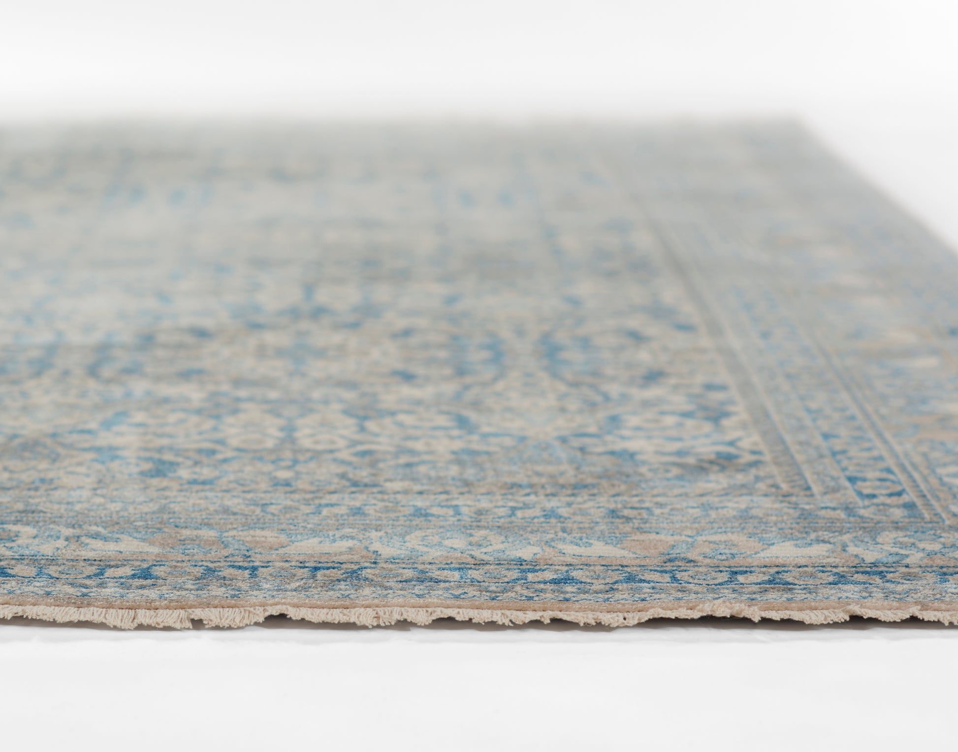Blue and beige oriental-style rug with a faded pattern and fringed edge.