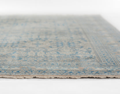 Blue and beige oriental-style rug with a faded pattern and fringed edge.
