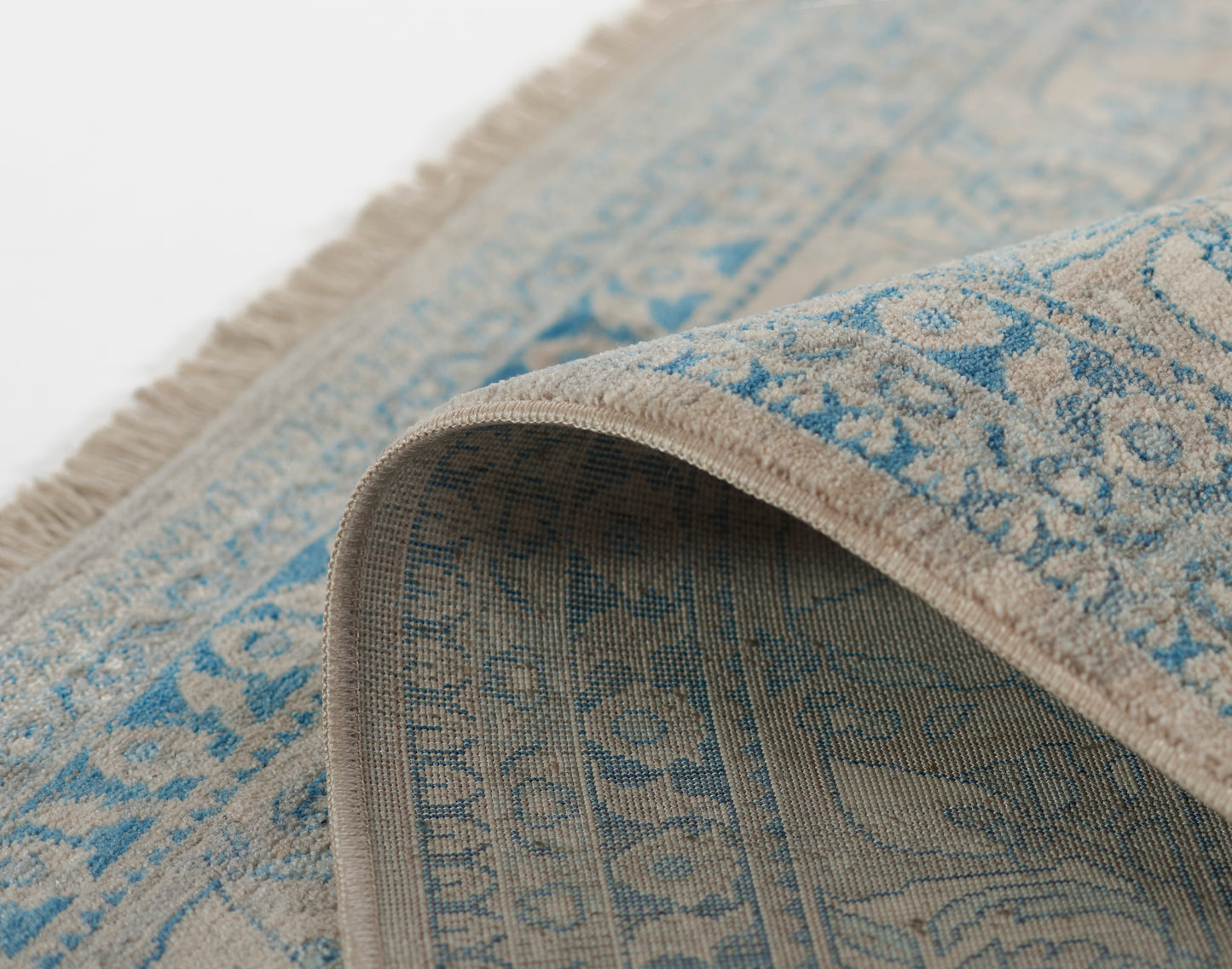 Blue & beige patterned woven area rug with fringed edges, partially rolled to show underside weave.