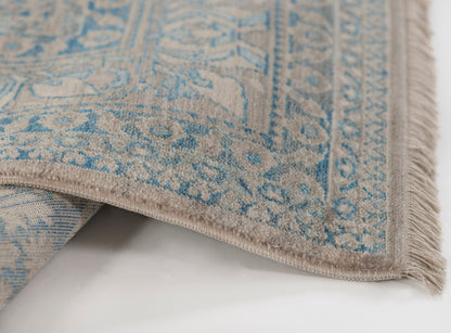 Blue and beige Turkish-style rug with an intricate oriental pattern and fringed edges, partially folded.