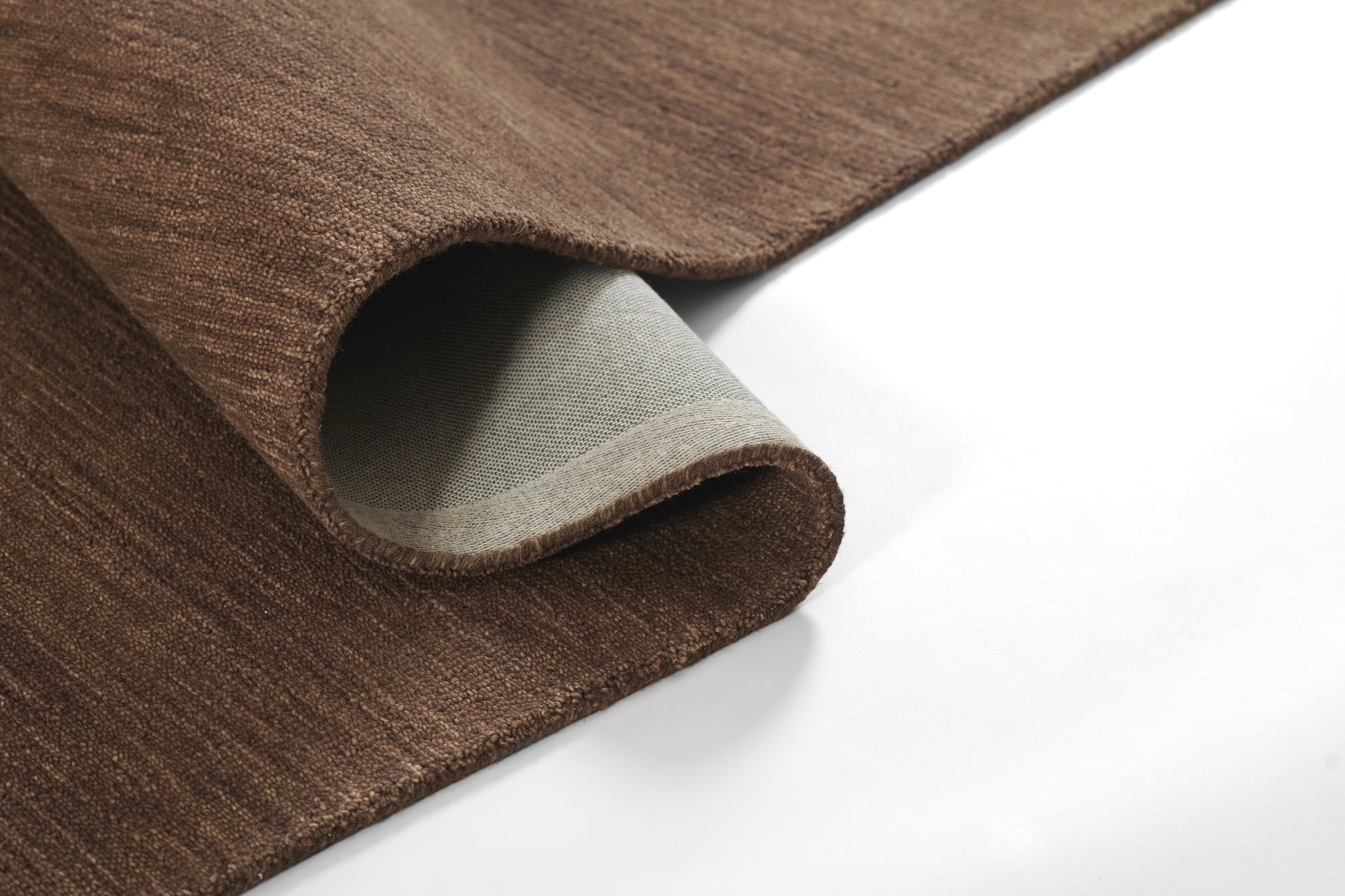 Close-up of brown faux leather rug with a curved edge exposing its gray backing.