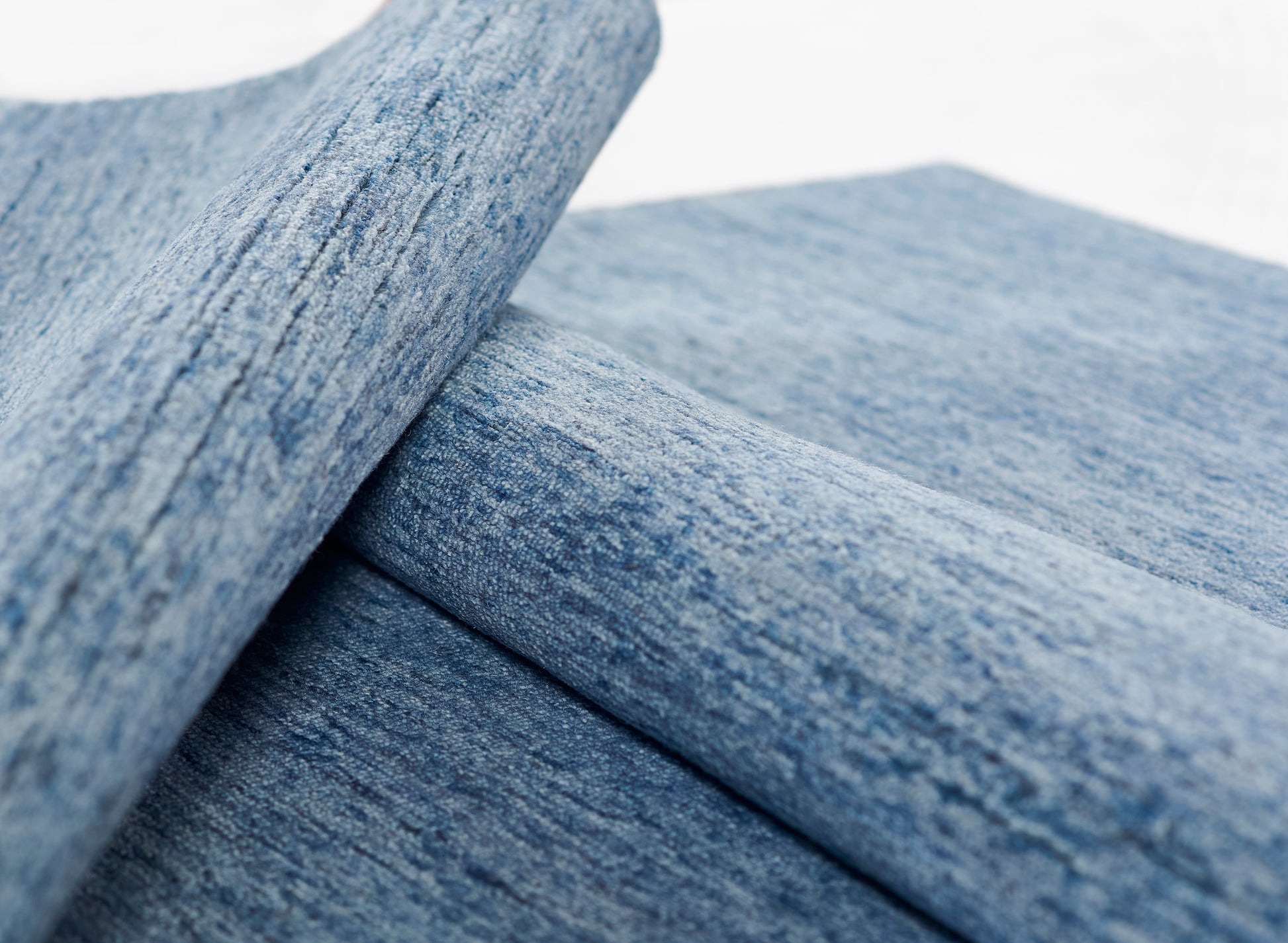 Close-up of light blue rug fibers with a denim-like texture and folded layers.