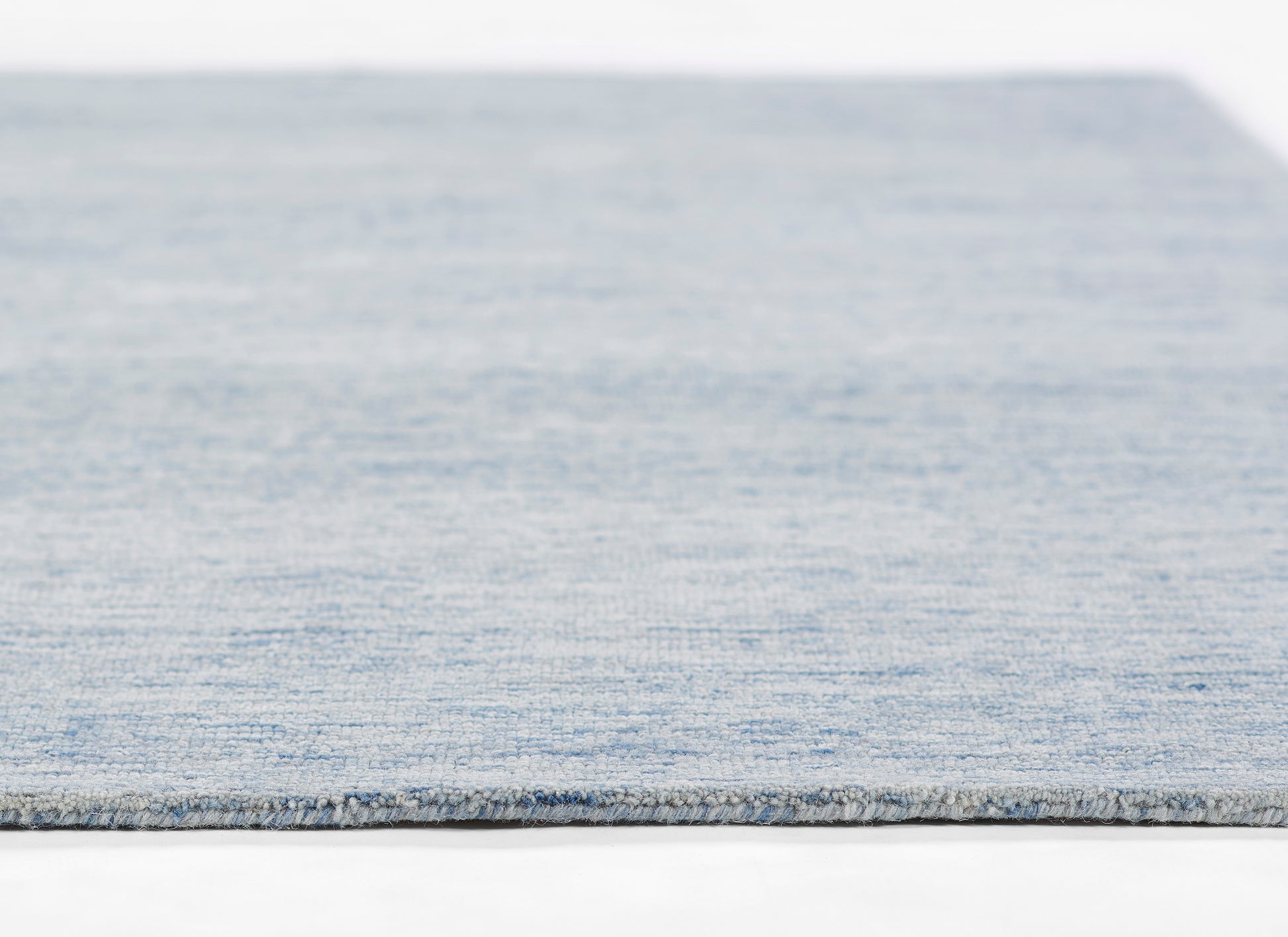 Light blue woven rug with subtle denim texture and gray binding edge.