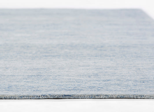 Light blue woven rug with subtle denim texture and gray binding edge.