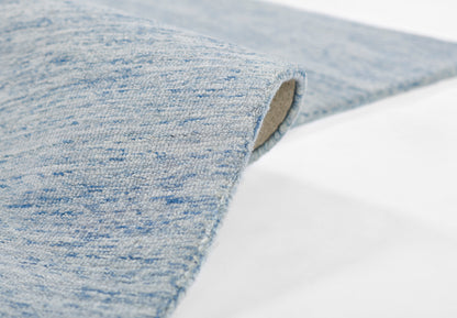 Light blue speckled woven rug, partially rolled edge, soft textured fabric, modern casual home decor accessory.