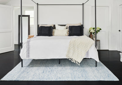 Light blue rug in a bright bedroom with a black metal four-poster bed, white bedding, a cream throw, and dark cushions.
