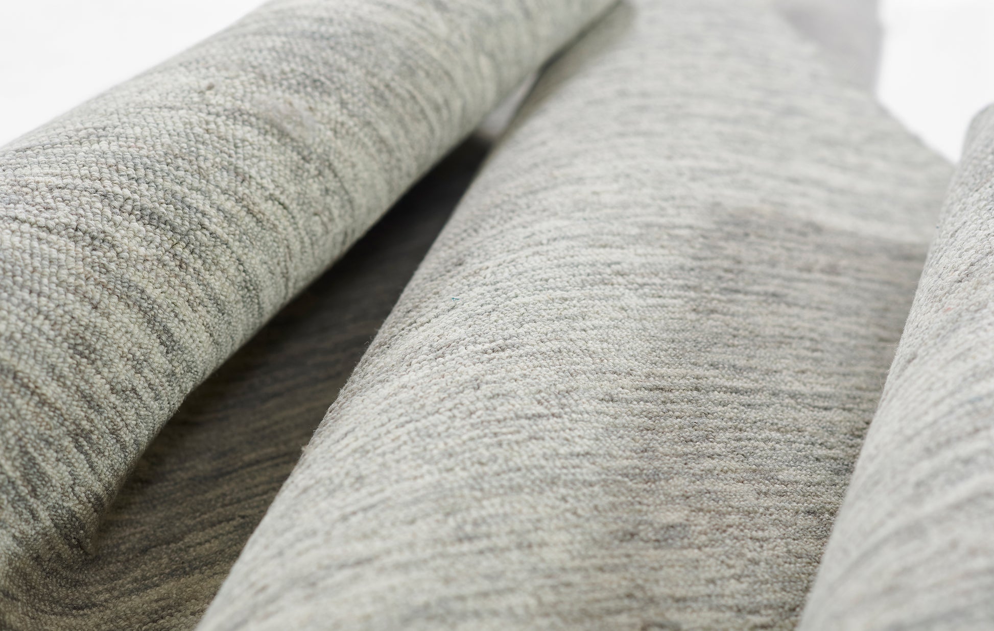 Close-up of light gray heather rug with soft texture and rolled folds.