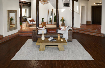 Rustic living room with dark wood floors, brown leather sofa, large wooden coffee table, beige area rug, and potted plants.