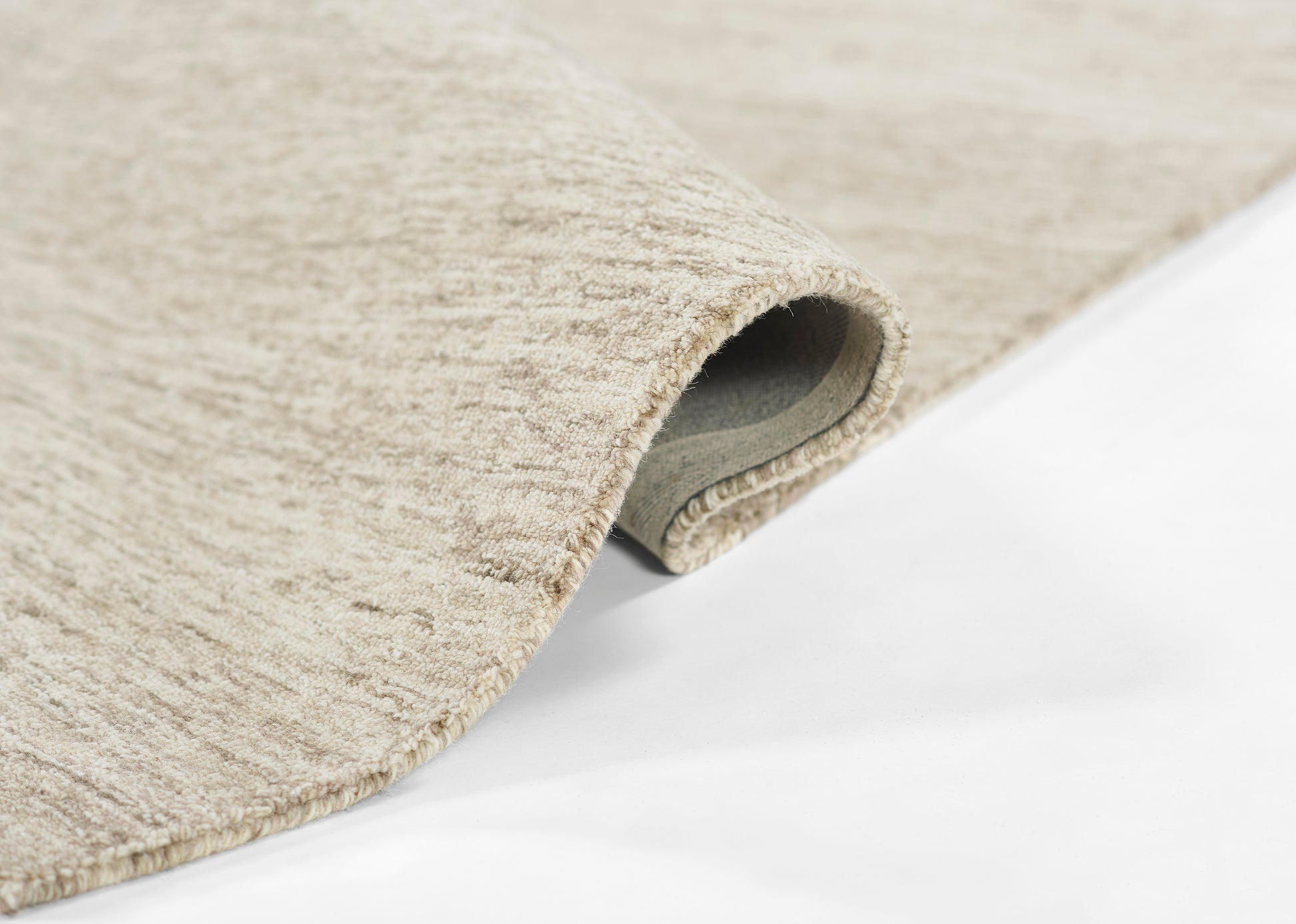 Natural beige rug rolled up to reveal underside; soft textured loop pile for neutral home decor.