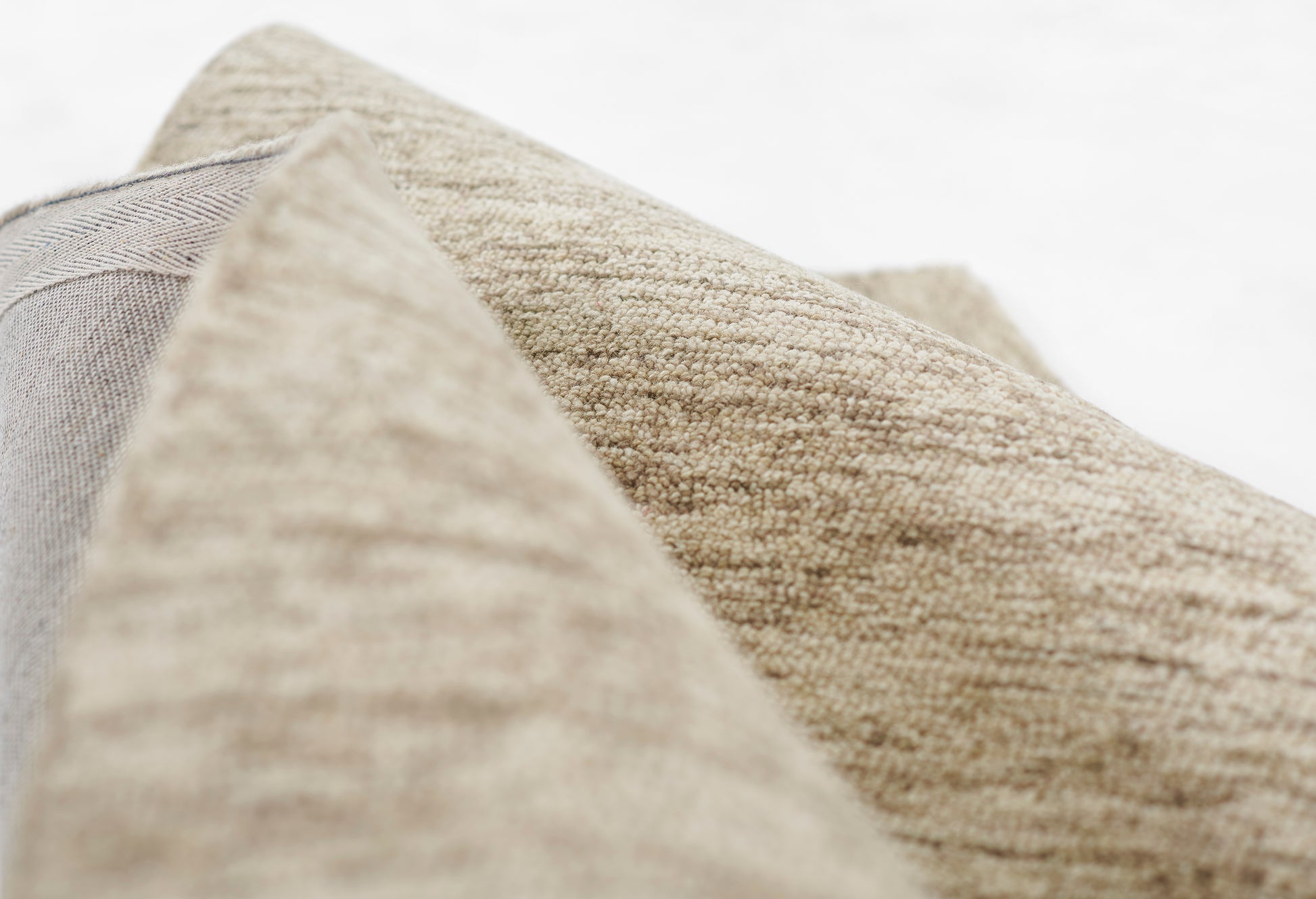 Beige textured woven rug close-up with folded edge, natural linen-like fibers, 8' x 10'.