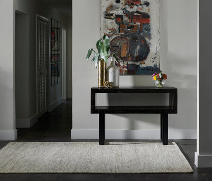 Black console table with glass top in entry hall, gold vases, green plant, abstract art, beige rug.