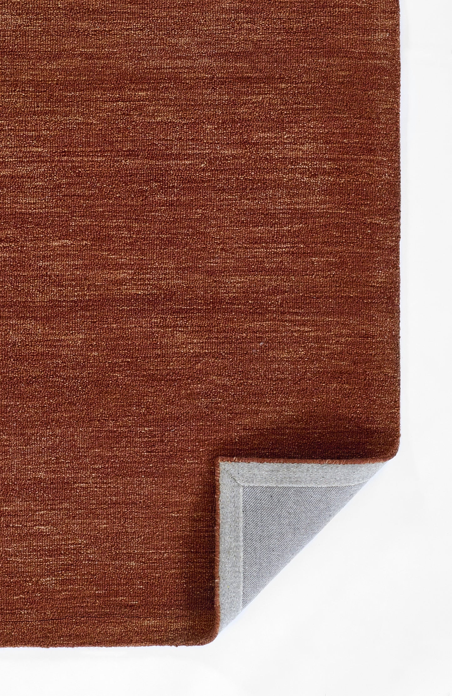 Rust-orange textured rug with woven pile; folded corner reveals light gray underside.