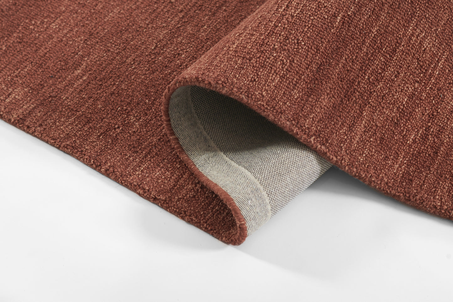 Rust-brown woven rug with textured pile; folded corner reveals light gray underside.