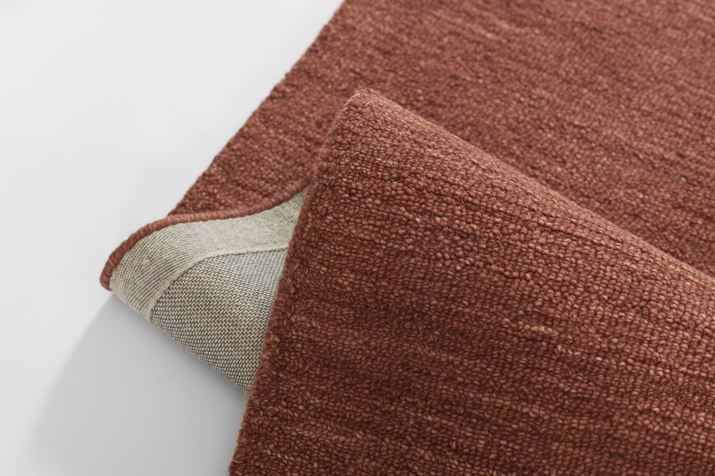Rust-brown textured rug with looped pile, folded to reveal beige underside.