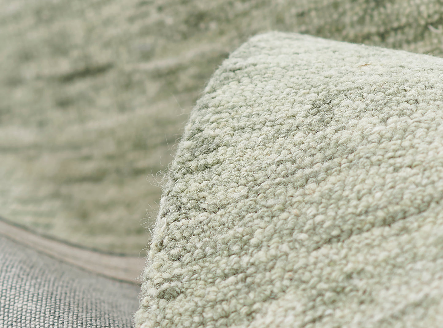 Sage green sherpa/bouclé fabric, close-up of soft textured throw blanket with a rolled edge.