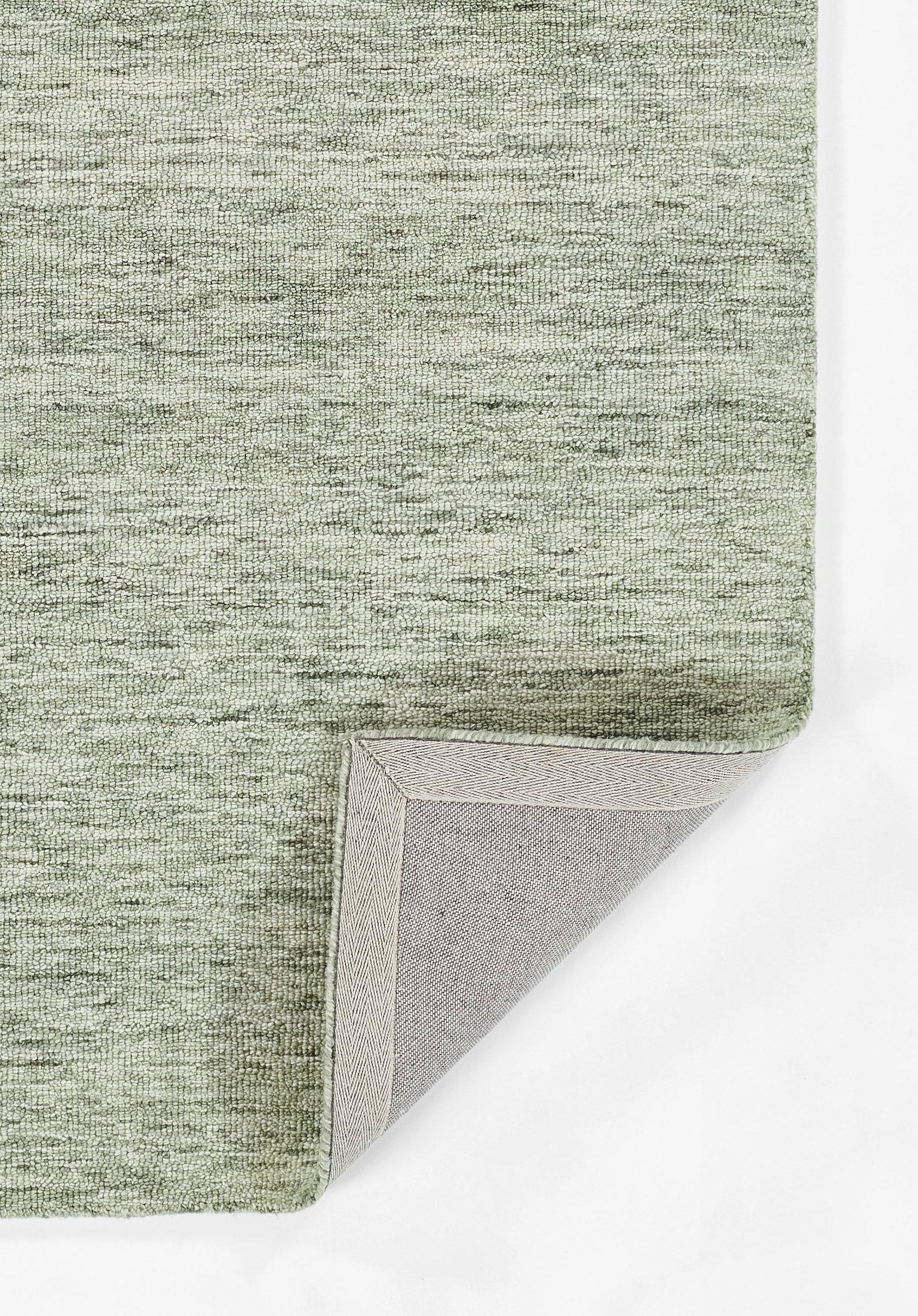 Sage green textured rug with a heathered weave and light gray backing visible at the folded corner.