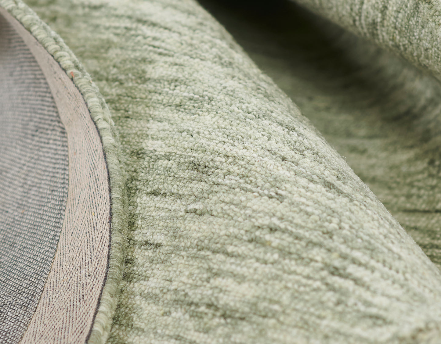 Close-up of sage green plush rug with soft loop pile and beige edging.